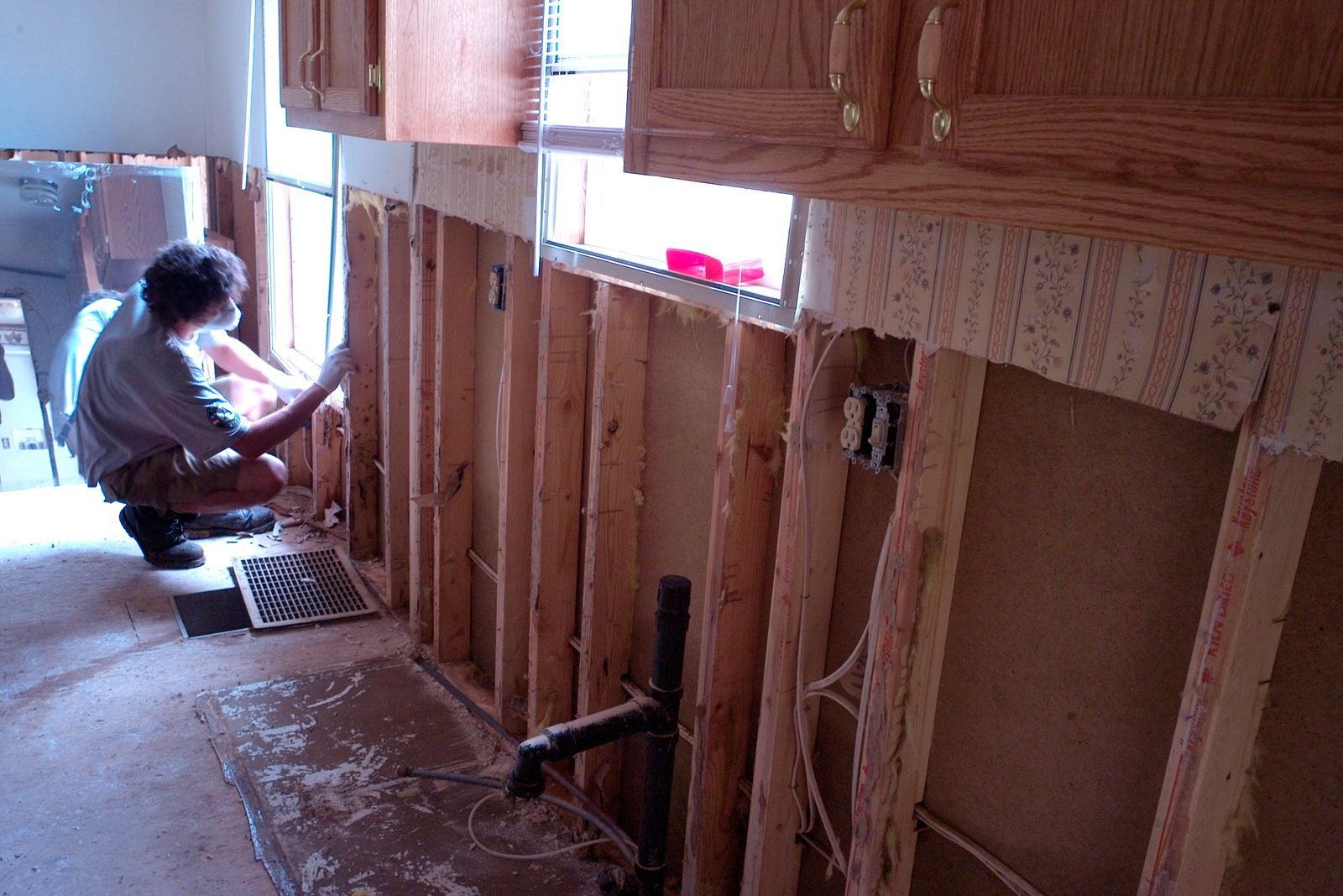 Kowalski Restoration technician in a respirator cutting wet drywall out of a kitchen wall after a flood, studs and wiring exposed