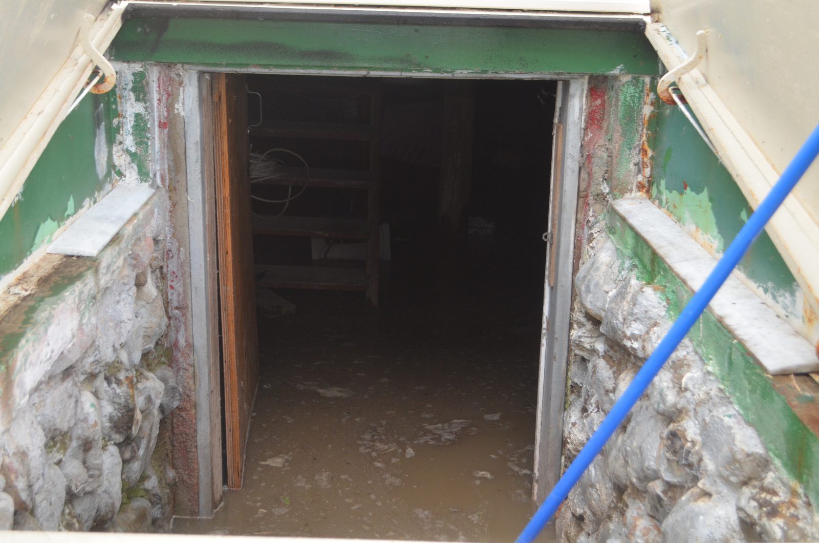 Open basement doorway with standing floodwater and a pump hose running down the stairs