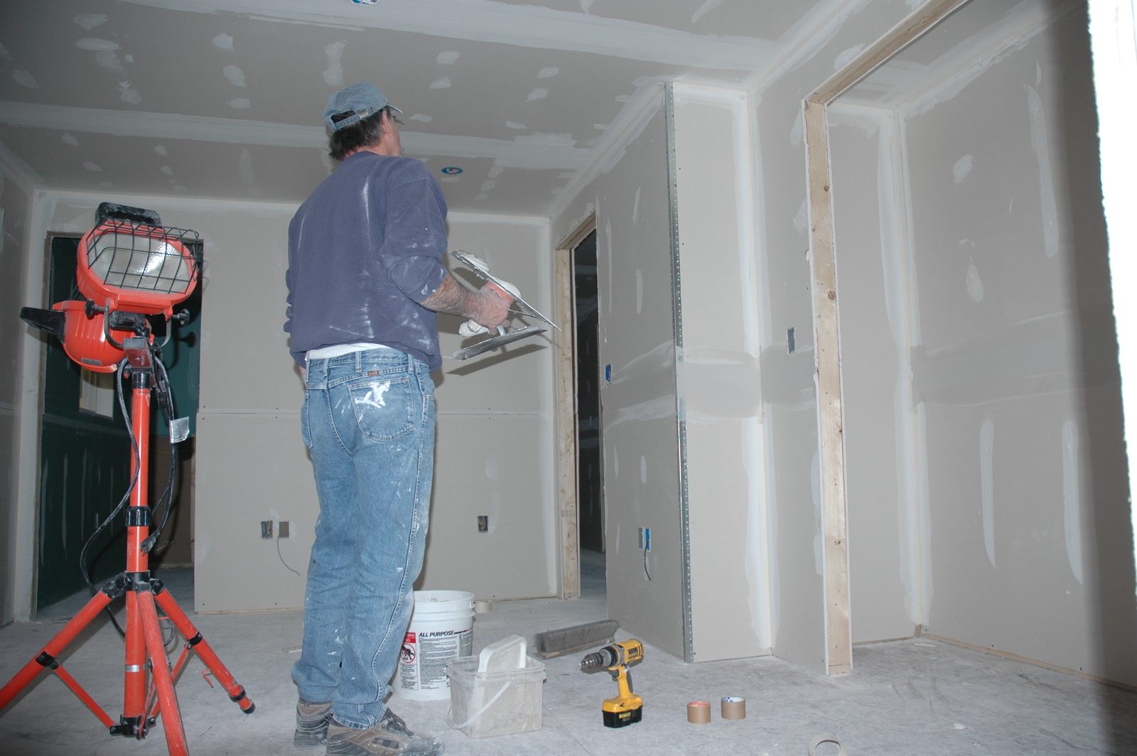 Technician finishing new drywall in a rebuilt room with a work light